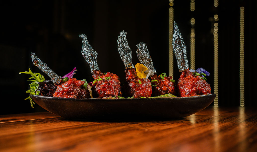 Glazed lollipop chicken with tall crisps, in a dark bowl at Chutneys