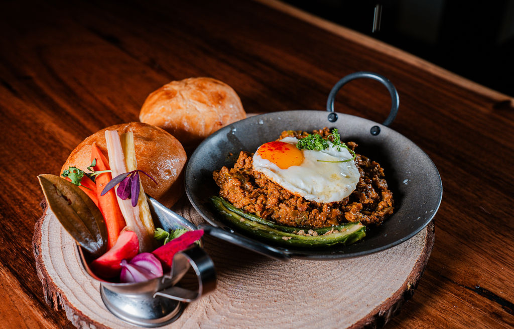 A skillet with a fried egg, pickled vegetables and soft buns on a wood board at Chutneys